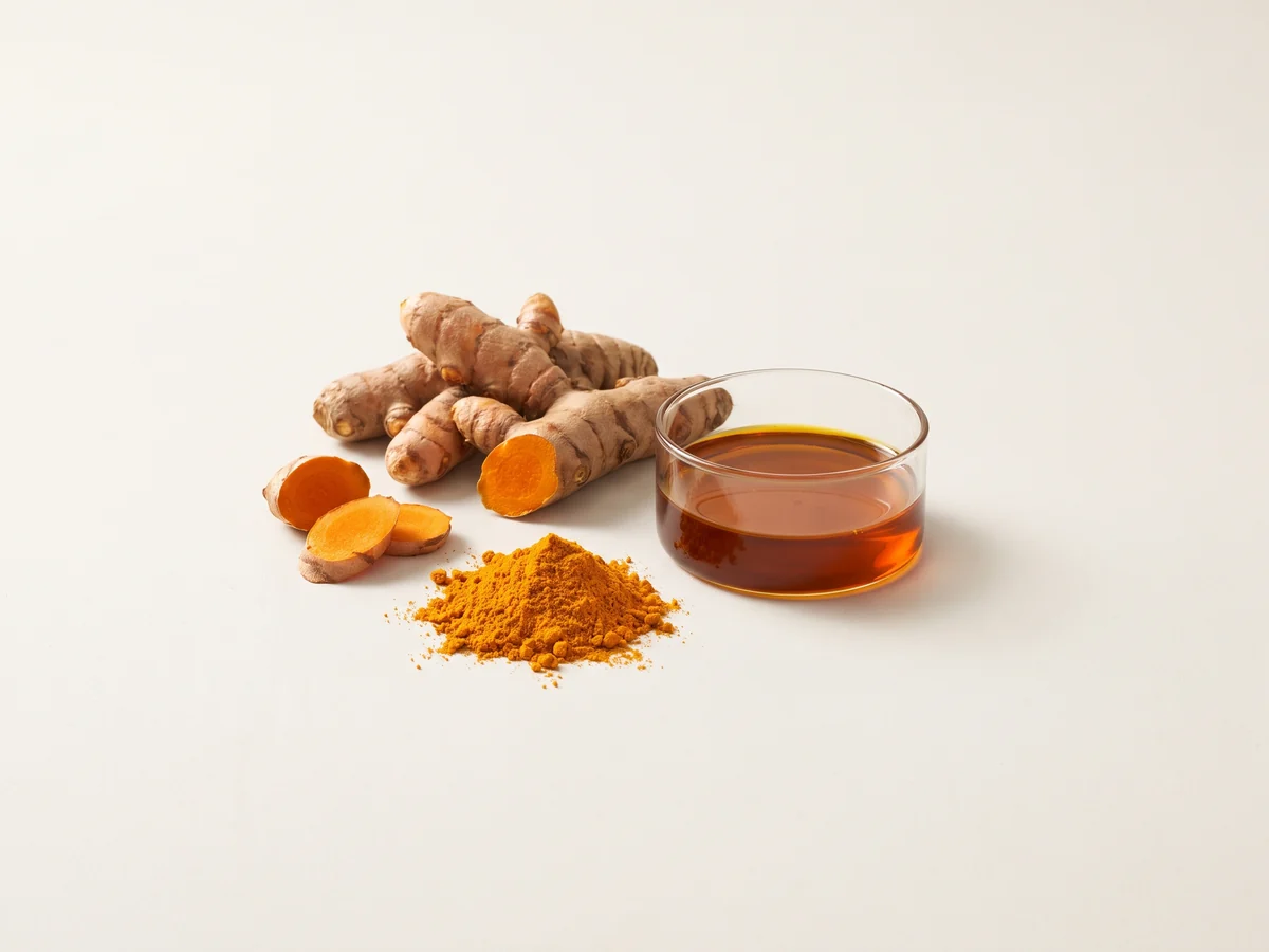 Turmeric roots and powder beside dark orange turmeric oleoresin in laboratory glassware
